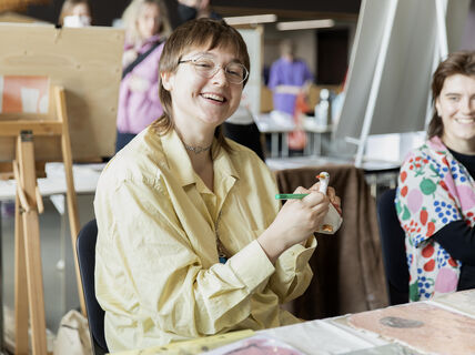Person in a yellow shirt holding a white figurine and green pen, sitting at a table with art supplies. Photo: Aalto University/Erica Nyholm
