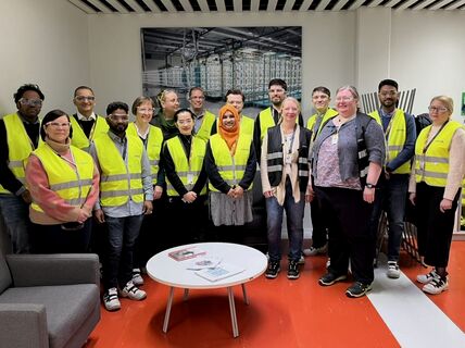 A group of people wearing yellow safety vests standing in an office with red flooring and a wall poster.