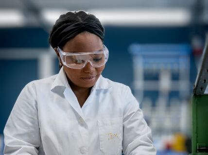 Person wearing a white lab coat and working with a machine in a laboratory or industrial setting.