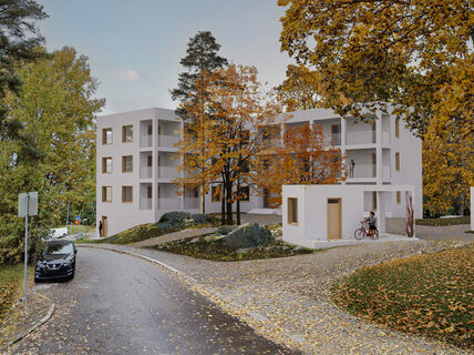 Modern white apartment building surrounded by autumn trees. A person rides a bike near a smaller white structure.