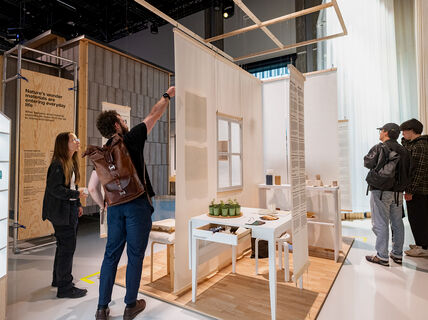 Visitors at an exhibition exploring sustainable materials. Displays include furniture, small plants, and design elements.