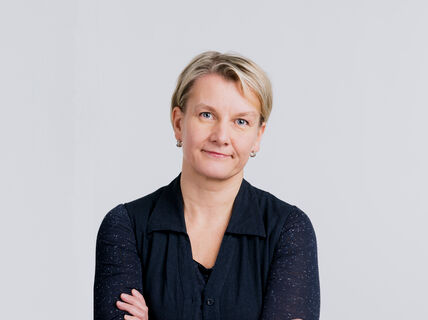 Woman with short blonde hair wearing a dark navy blue long sleeve shirt, arms crossed.