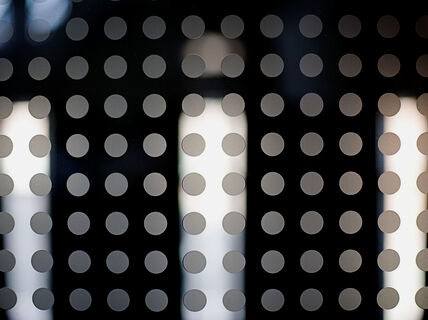 Mönstrat glas med jämnt placerade grå prickar i rader, med vertikala ljusa lampor synliga bakom.
