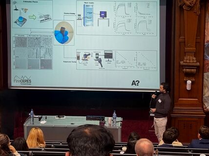 A person is presenting slides in an auditorium. The audience is seated. The presentation title reads 'FinnCERES'.