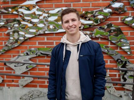 Oskari Heikkilä in front of a brick building with metal art pieces