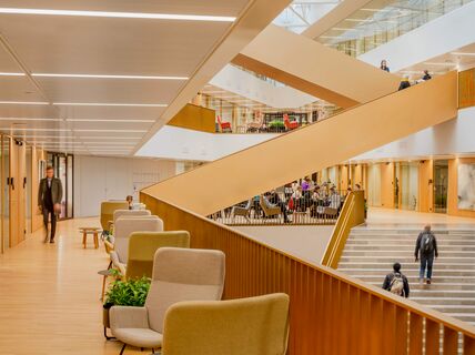 Picture from Aalto University's School of Business. The space has wooden floors, stairs, comfortable seating and people walking and sitting.