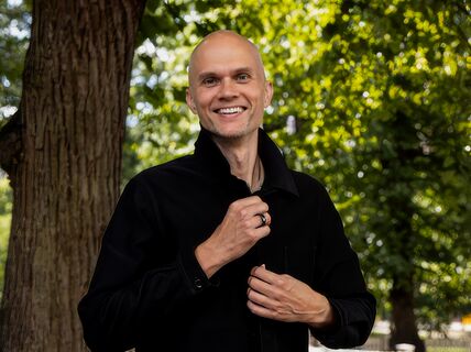 A person wearing a black shirt stands outside near a tree.