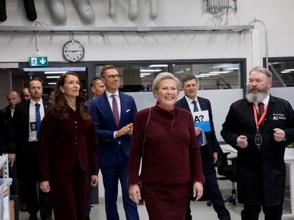 Group of people touring a modern office space with a clock on the wall and various equipment visible.