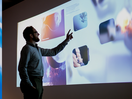 A person points at a projection screen displaying various images and text.