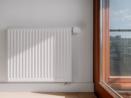 White panel radiator on a light wall beside a wooden-framed glass door with city view