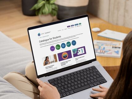 Person on a sofa using a grey laptop to browse a colourful online student course catalogue
