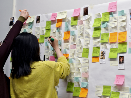 Three people add notes to a white wall filled with colourful sticky notes and small printed photos