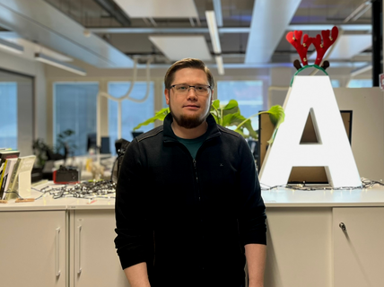 Man in dark clothes in modern office, standing by large lit letter A with red antlers and plants behind