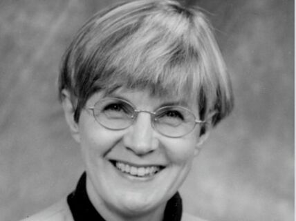 Paula Nybergh. Mustavalkoinen muotokuva hymyilevästä lyhyttukkaisesta naisesta, jolla on silmälasit ja vaalea takki.