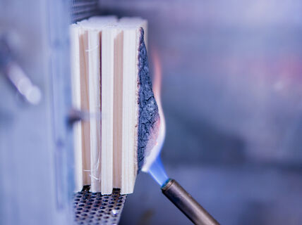 Blowtorch flame charring the side of stacked wooden boards in a metal test rig