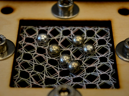 Metal balls on a geometric thread lattice framed in light wood with four silver screws