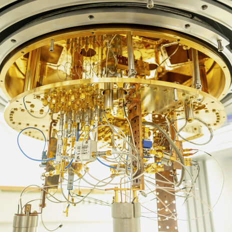 A gold-plated cryostat sits half open with many cables coming out from the bottom.