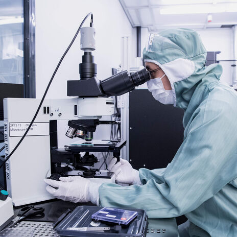 A researcher in protective gear working with a microscope in a laboratory.