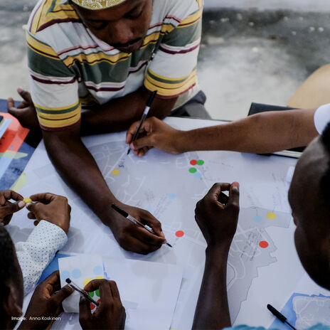 Group of people working on a map with coloured dots, using pens and notebooks at a table.