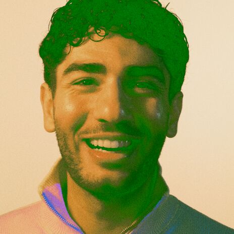 Henkilö, jolla on vaalea vetoketjullinen villapaita ja kaulakoru, yksiväristä taustaa vasten.