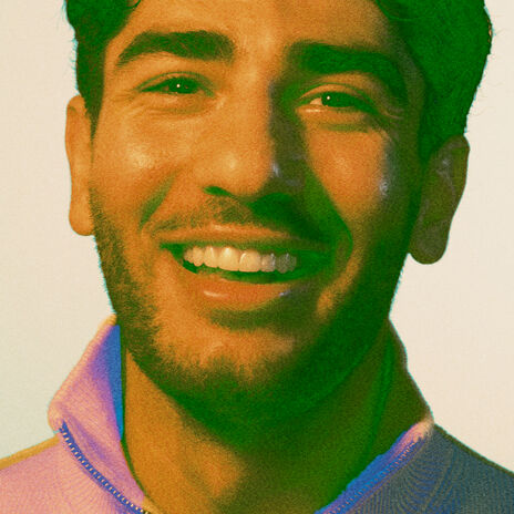 Henkilö, jolla on vaaleanvioletti vetoketjullinen takki, vaaleaa taustaa vasten.