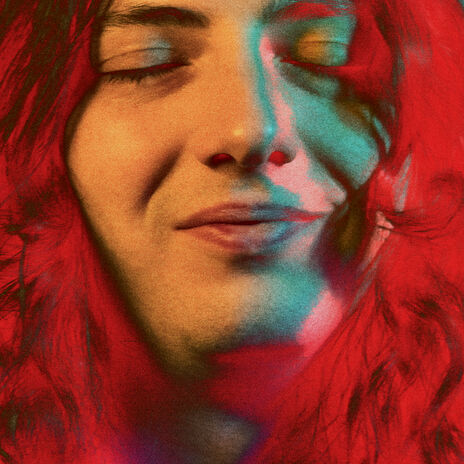 A reddish-toned photograph of a long-haired man smiling with his eyes closed.