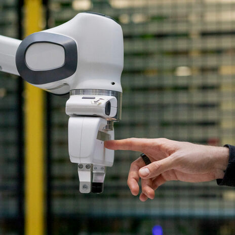 Human hand touches white robotic arm’s gripper in an indoor industrial setting