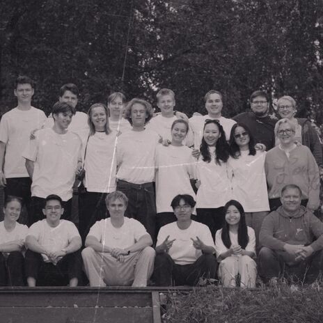 Black and white group photo of smiling people in light tops outdoors, posing on wooden steps