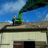 Thumbnail of A worker in safety gear on an old tiled roof under a blue sky.