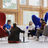 Thumbnail of Four people having a discussion in a modern room with large windows. They sit on colourful chairs and cushions around small tables.