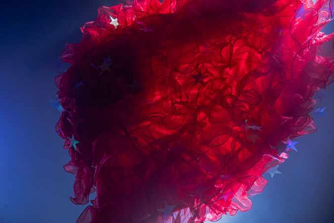 Close-up of flowing red ruffled fabric with scattered star shapes, lit by blue and pink light