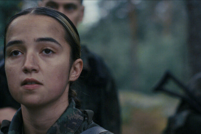 Soldiers in camouflage uniforms stand in a forest, faces blurred, one holding a dark rifle.