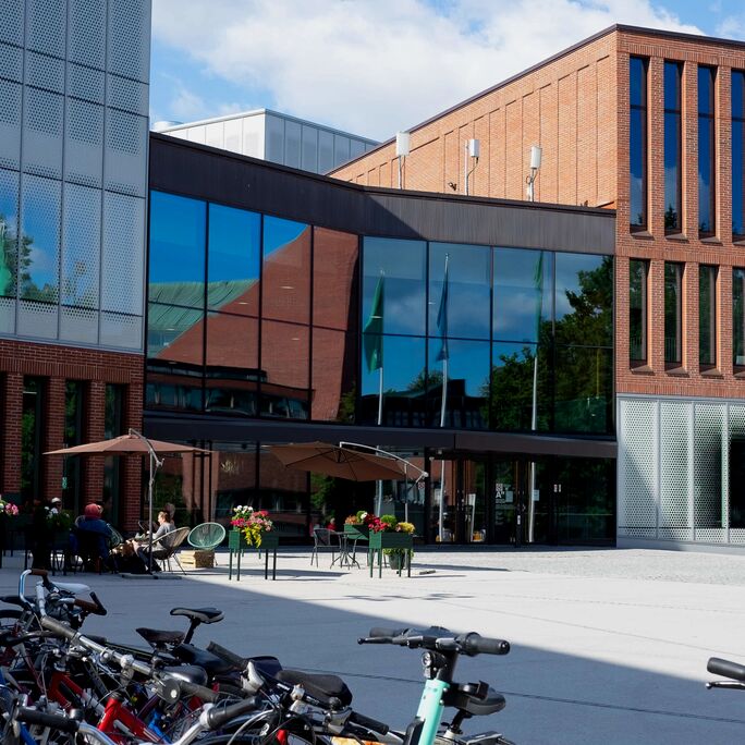Moderni rakennus, jossa lasi-ikkunat ja tiiliseinät Aalto-yliopistossa. Polkupyöriä parkissa etualalla.