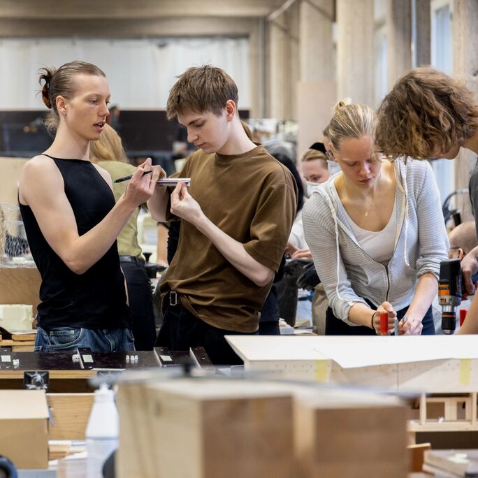People working on architectural models in a studio, with various tools and materials on the tables.