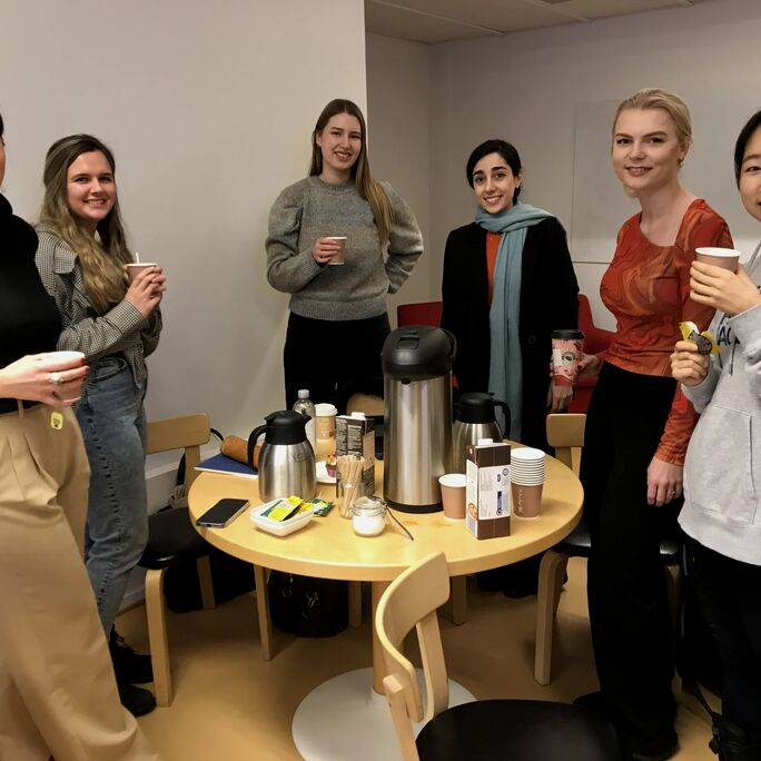 A group of people standing around a table with coffee and snacks in a casual setting.