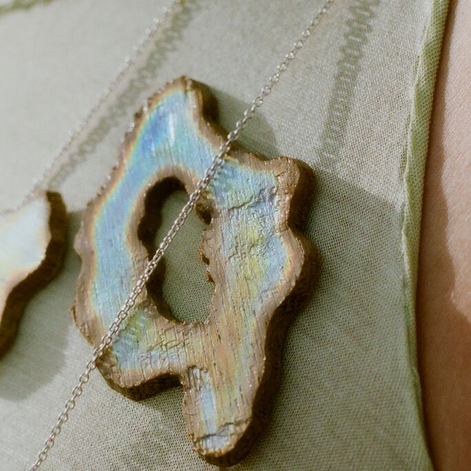 Close-up of a person wearing necklaces with iridescent wooden pendants on a light green fabric.