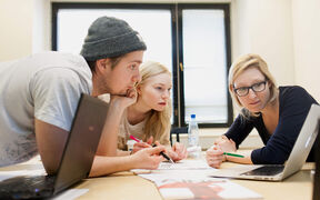 A group of three students engaging in teamwork, one presenting something from her laptop's screen