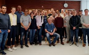 A large team standing and team leader sitting in front of the team.