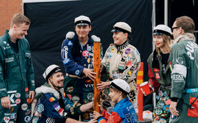 A group of seven students in their colofurful overalls, playing a game in Aalto Party