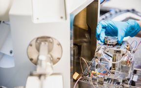 A hand with a blue vinyl glove adjusts complicated research instruments.