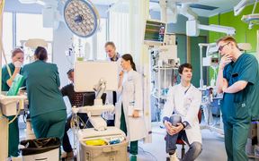 Seven people wearing laboratory coats in a hospital room surrounded with medical devices