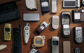 A collection of various old mobile phones laid out on a wooden surface.