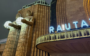 Close-up of Helsinki Central Station with two stone statues holding spherical lamps and the sign 'RAUTA'.