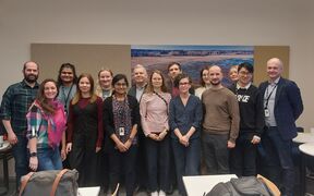 Yksitoista ihmistä seisoo toimistossa, joillakin on henkilökortit. Taustalla on seinätaidetta.