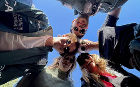 Kuvassa näkyy viisi opiskelijaa aurinkolasit päässä. Opiskelijat seisovat kehässä, ja kuva on otettu sen keskeltä alhaalta päin. 