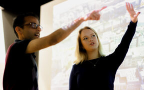 Two people discussing a map projected on a wall, pointing towards different areas.
