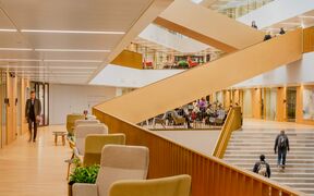 Kuva Kauppakorkeakoulun sisätiloista. Tilassa on puulattiat, portaat, mukavat istuimet ja ihmisiä kävelemässä ja istumassa.