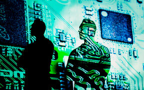 A person silhouetted against a green-lit circuit board projection facing forward.