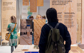 Ihmiset tarkastelevat puupintoja ja 3D-tulostettuja rakennusmateriaaleja näyttelyssä.