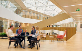 Business school main building. Students sitting around a table and working on their computers.